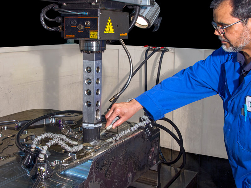 A toolmaker is adjusting settings on EDM machine where an electrode is burning its shape on a mould