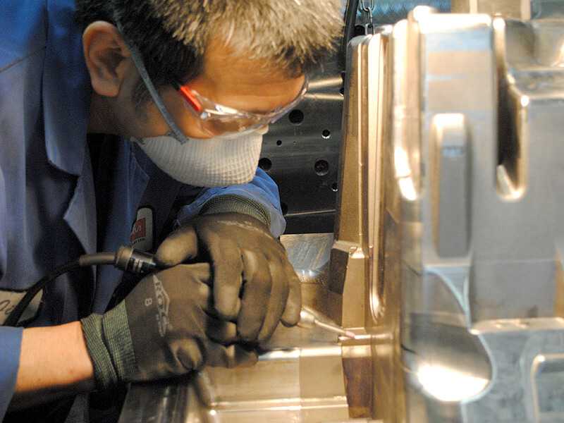 Screen shows a toolmaker grinding detail work on a finished mould with a pencil grinder